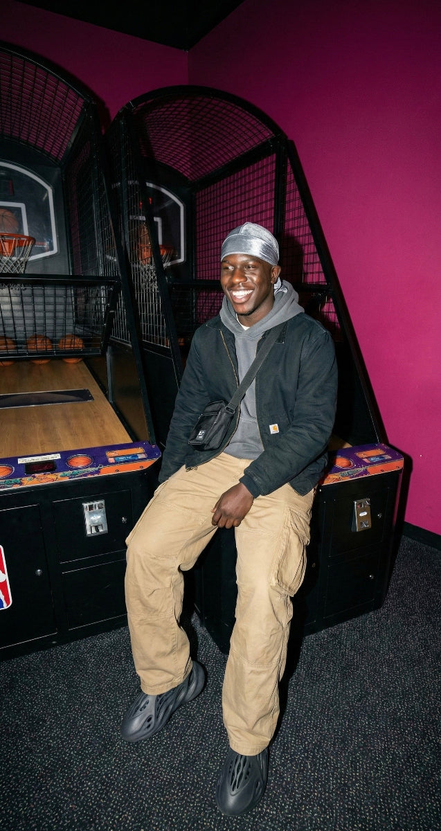 Person sitting on a vintage basketball arcade machine with a grey durag